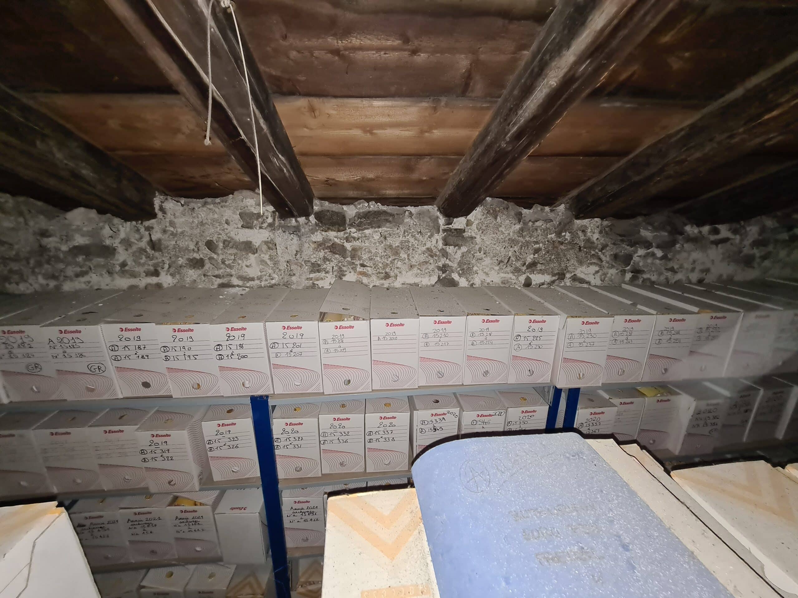 Boîtes d'archives empilées dans un grenier en pierre.