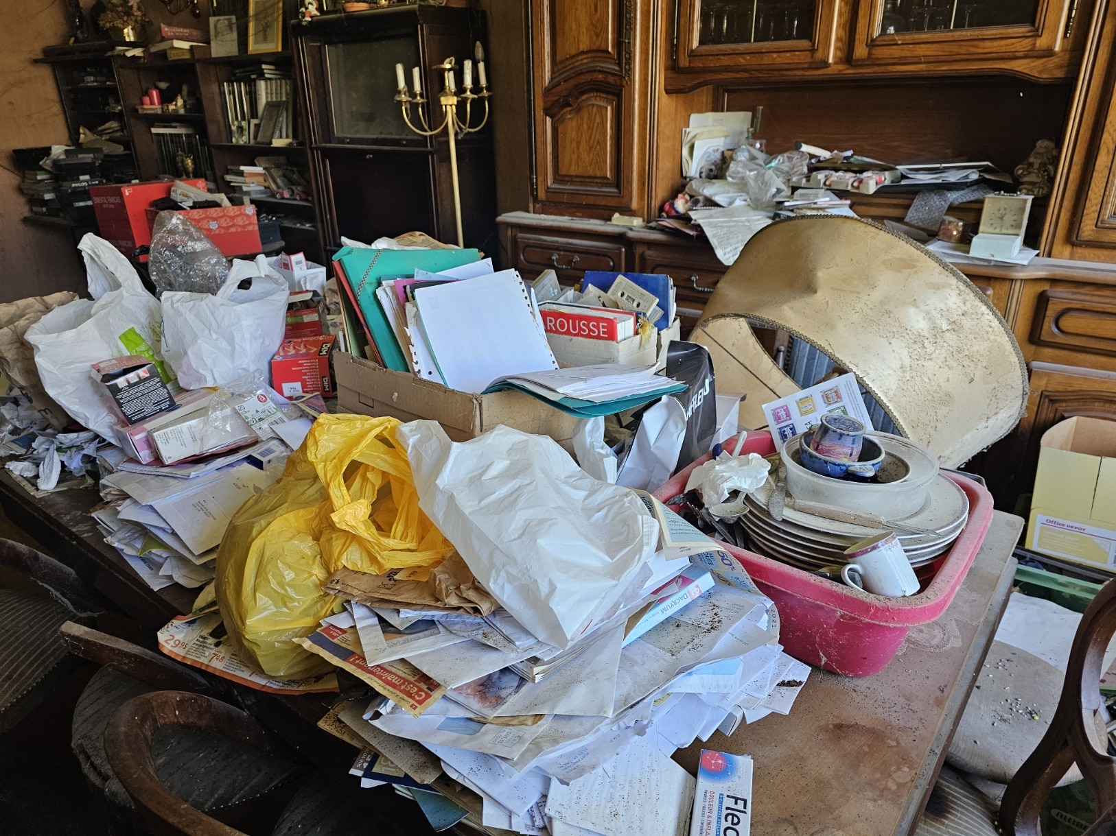 Salon encombré avec piles de papiers et objets divers.