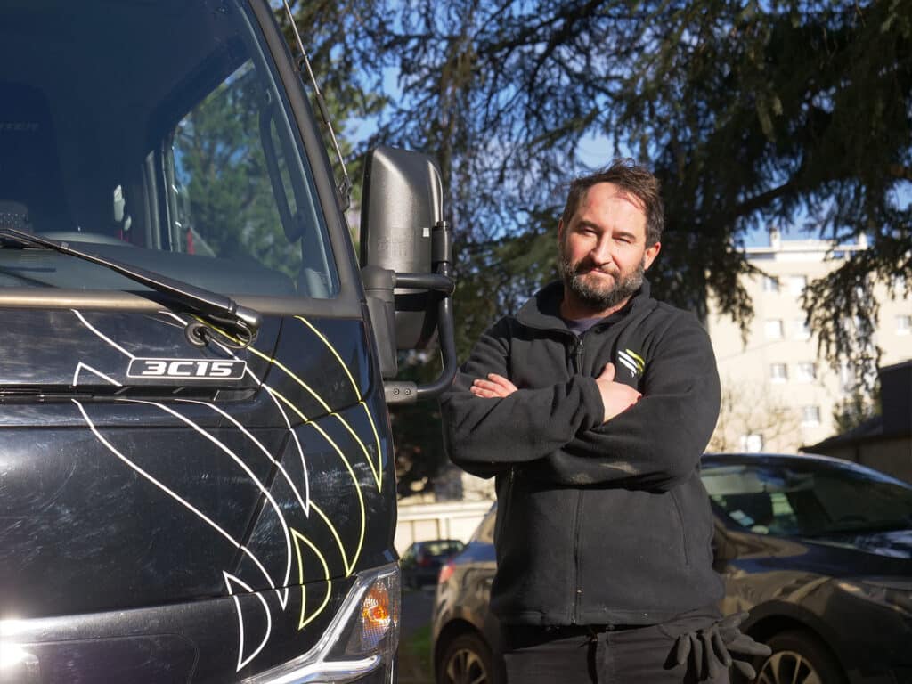 Personne posant à côté d'un véhicule noir.