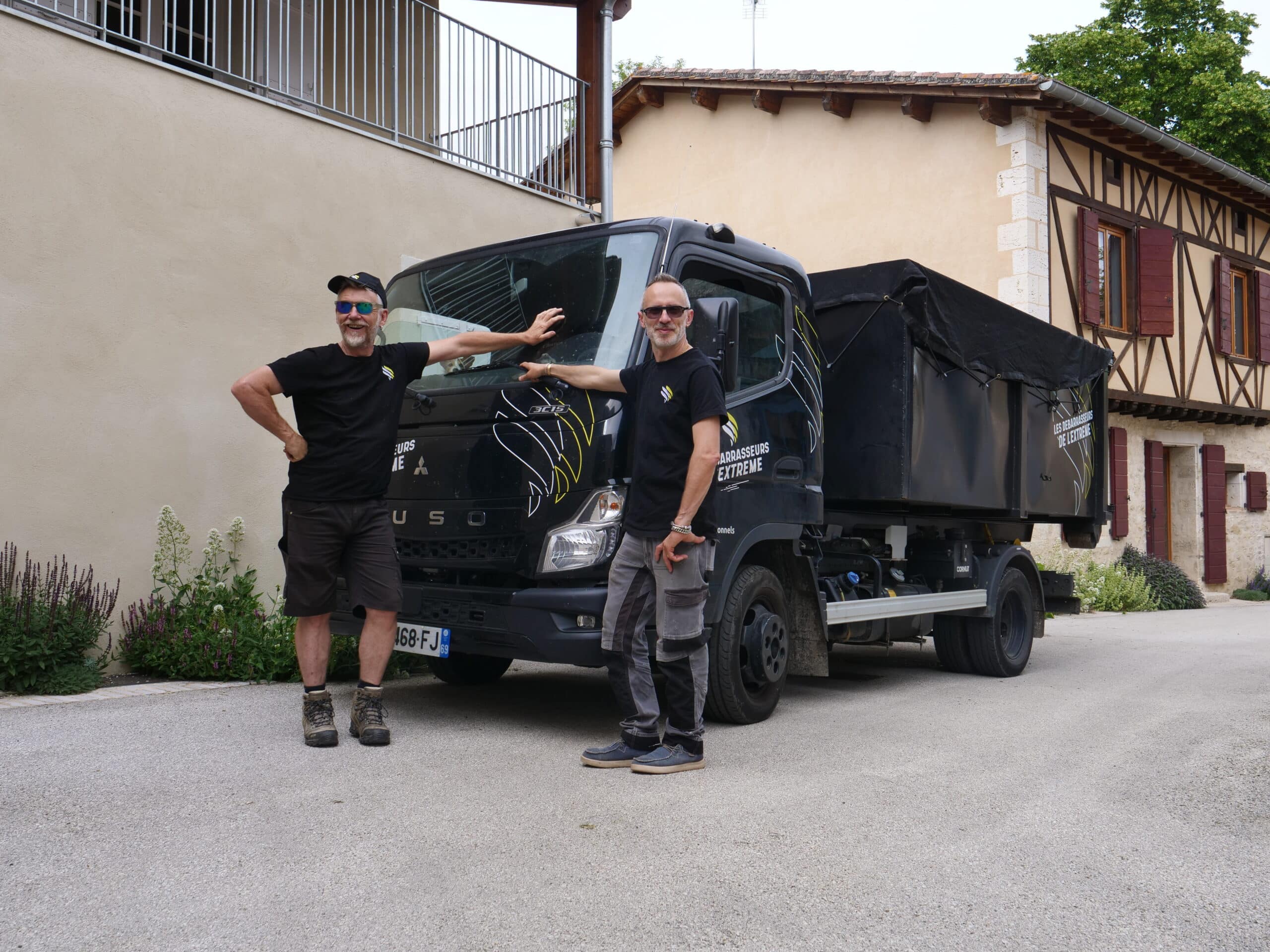 Deux hommes posent devant un camion noir.
